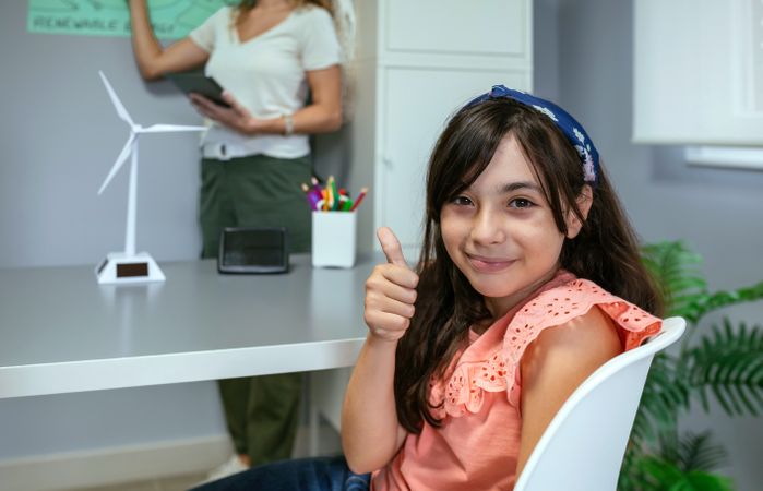 Portrait of schoolgirl in ecology classroom and teacher explaining lesson on background