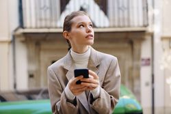 A Thoughtful Young Woman Utilizing Her Smartphone While Enjoying the Outdoors in Daylight