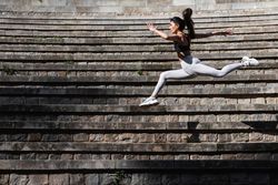 Flexible woman jumping above stone stairs