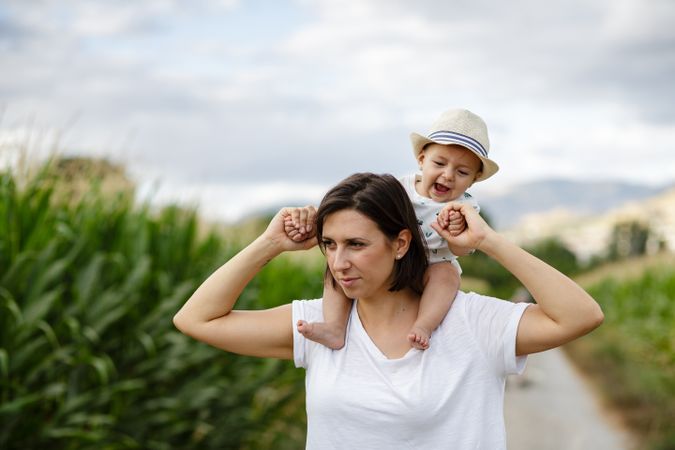 Adorable kid in hat on shoulders and looking at mother