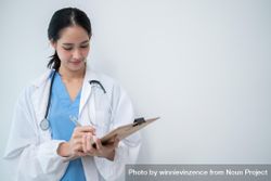Doctor standing in bright hospital room writing in clipboard with copy space 5wBJ10