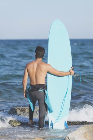 Male surfer with blue board enjoying the view of the water from rocky shore