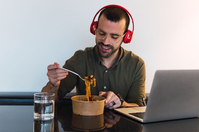 Positive man in headphones eating noodles