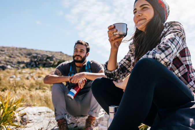 Young woman drinking coffee and resting with friend during hike