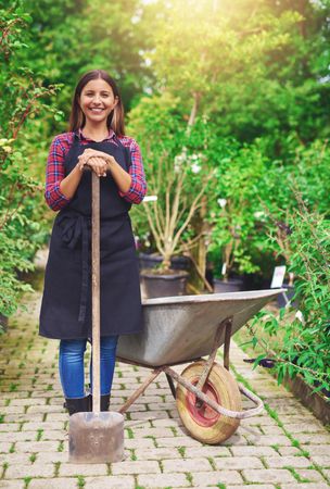 Smiling florist pictured with wheelbarrow and shovel in a greenhouse