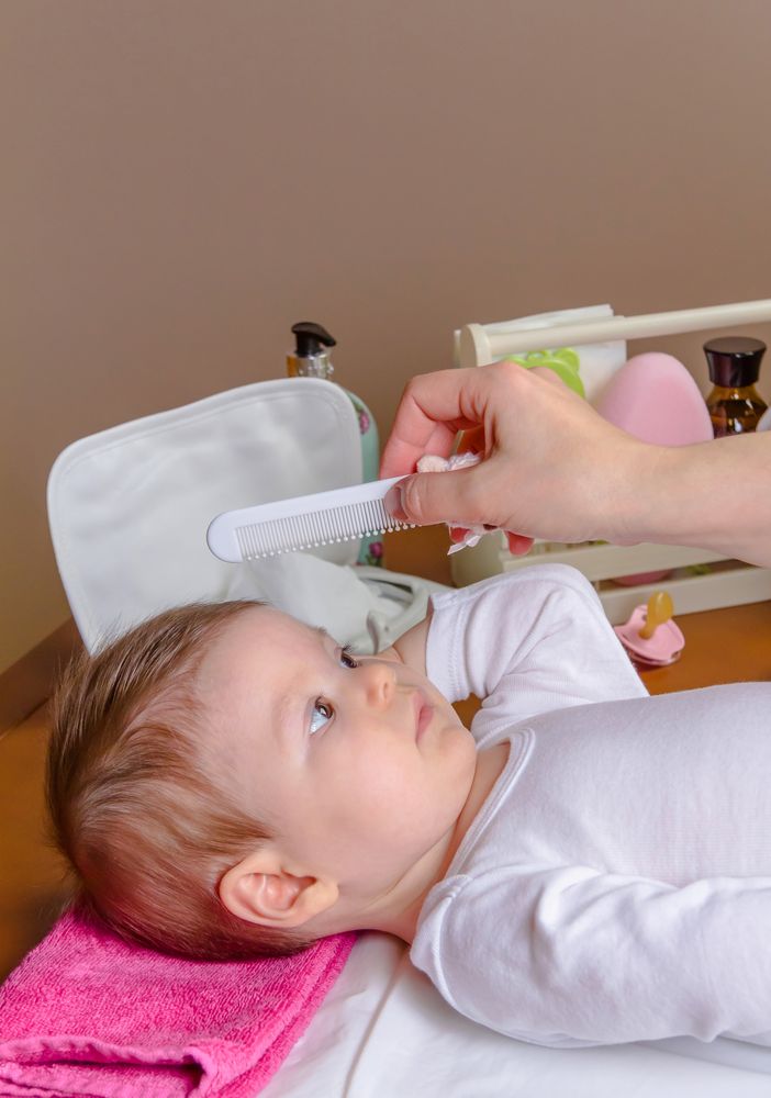Mother grooming hair of baby with comb