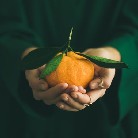 Woman in green holding tangerine with both hands, square crop