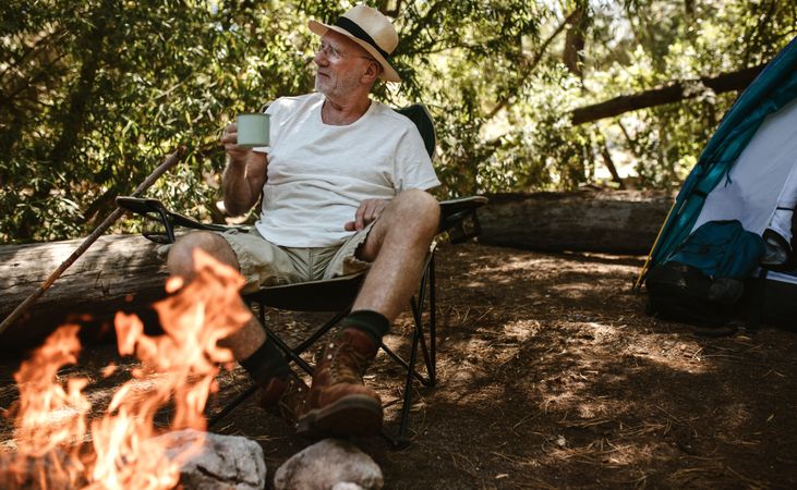 Retired man sitting near campfire and having coffee