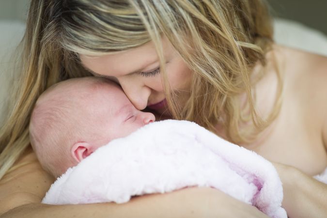 Young Mother Holding Her Small Newborn Baby Girl To Her Face