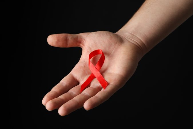 Hand and red awareness ribbon against dark background, space for text
