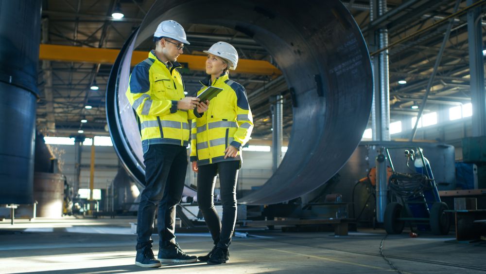 Male and Female Industrial Engineers in Hard Hats Discuss New Project while Using Tablet Computer.