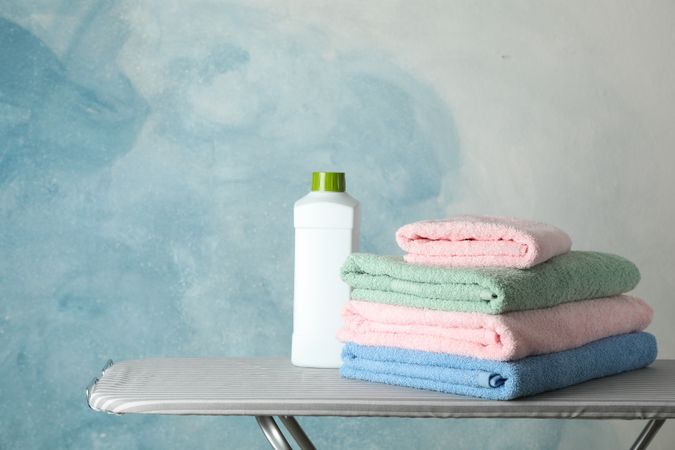 Stack of clean towels and laundry liquid on ironing board, copy space