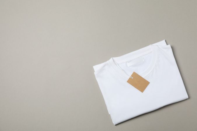 Folded blank plain t-shirt with tag on gray background, space for text