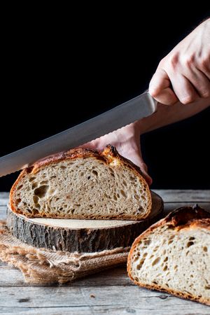 Crop person cutting country sourdough bread
