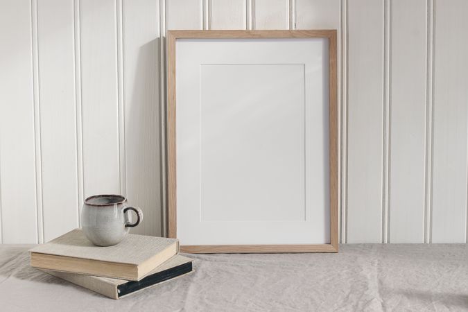 Blank vertical wooden picture frame mock up on linen table cloth. Modern interior. Cup of coffee on pile of vintage books.