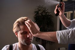 Barber spraying hair of client in barbershop