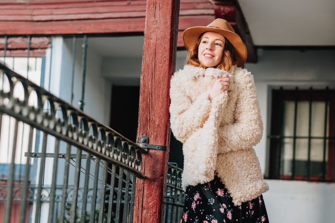 Smiling woman in warm wear standing near building and fence