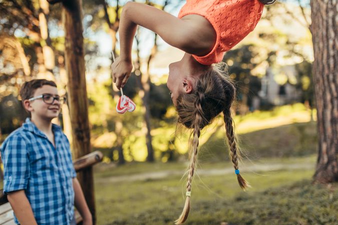 Girl hanging upside down in a park holding a heart shaped candy lollipop