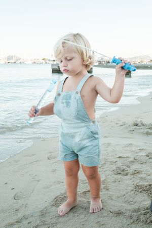 Serious curious toddler playing with soap bubble toy on beach in