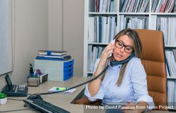 Busy businesswoman talking between two phones in office bYqw16