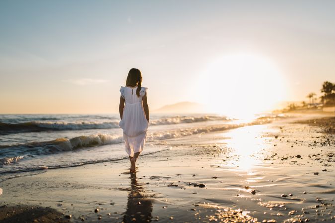 Adorable girl walking on seaside at sunset