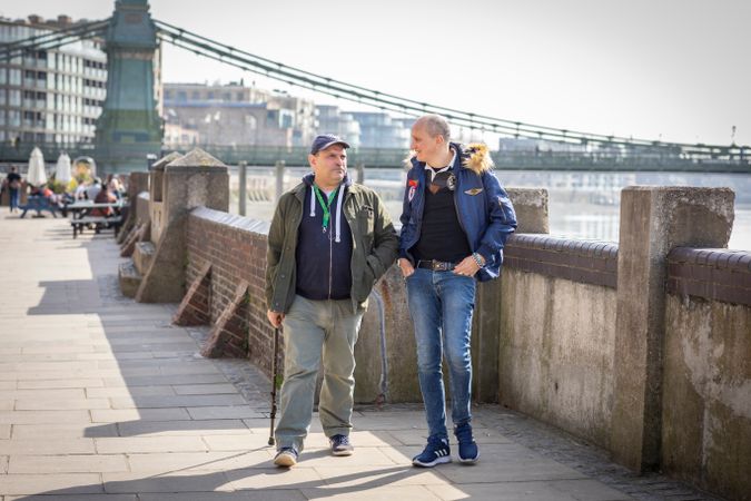 Two male friends walking by the river and talking