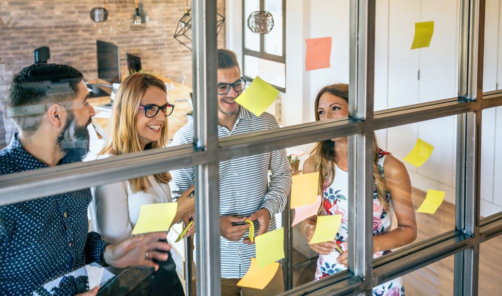 Happy business people in a work meeting placing sticky notes on the wall