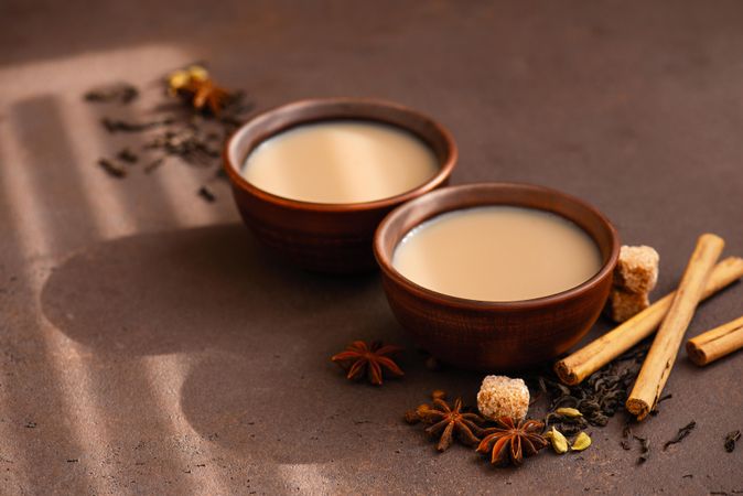 Two cups of chai tea pictures with anise, cardamon and cinnamon