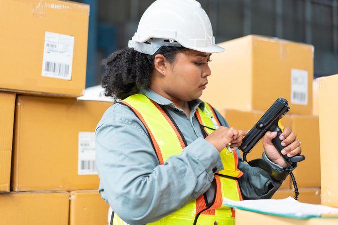 Woman in safety gear working in warehouse checking bar codes on boxes