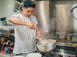 Asian male pouring soup in kitchen