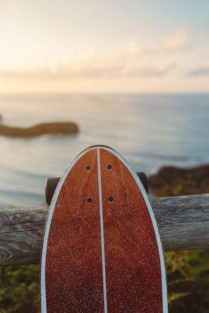 Surf skate leaning on wooden railing against blurred beach