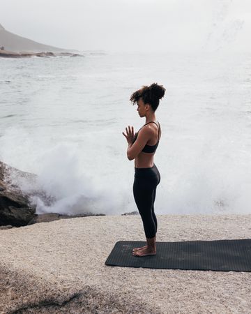 Female standing with hands together in prayer pose next to the ocean