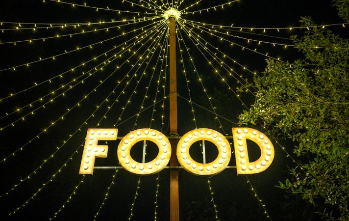 Signboard with word food made with light bulbs hung on wooden post under light garlands