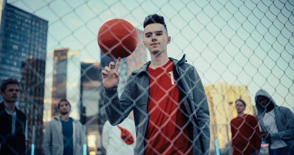 Portrait of a Young Football Player Looking at Camera, Spinning a Red Soccer Ball on His Finger.