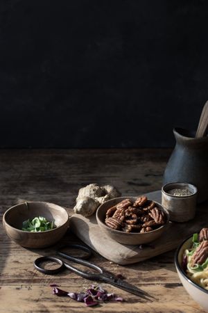 Bowl with pecan nuts near scissors, cutting board, pitcher and ginger
