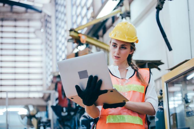 Woman in manufacturing factory in hard hat and laptop