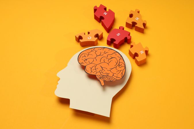 Paper cut out of head with brain & puzzle pieces on orange background