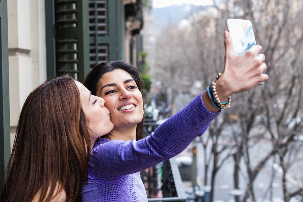 Happy lesbian couple taking selfie on balcony