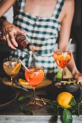 Young woman in checkered dress pouring aperitif with orange slices