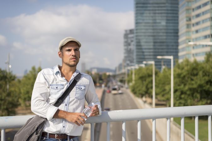 Relaxed male in denim with city traffic below standing on bridge