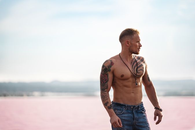 Undressed muscular man walking on shore of pink lake