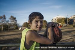 Young teen male with sleeveless shirt standing on a street basket court while smiling at camera 4MQO14