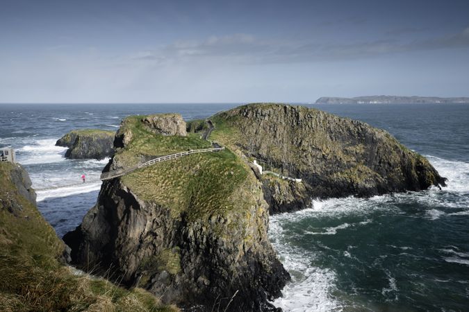 Tourist walking on rope bridge suspended between cliffs in Northern Ireland