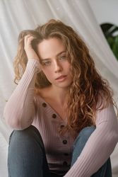 Charming woman sitting near curtain and daydreaming