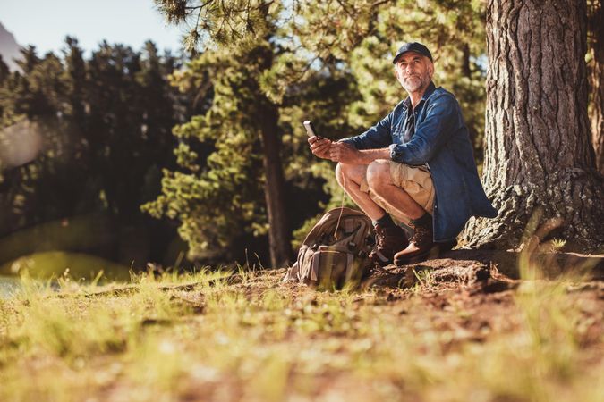 Portrait of an older man sitting outdoors in forest with a compass