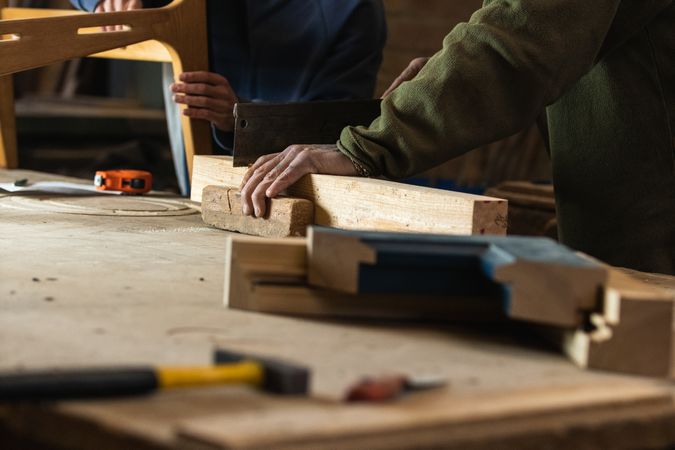 Joiner cutting wood with colleague measuring height