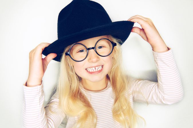 Smiling blonde girl holding her hat and wearing glasses