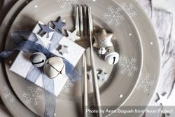 Top view of wrapped Christmas present with bell and star ornament on table setting 5XRdQb