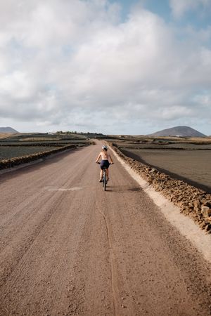 Back of female biking on Lanzarote dirt road, vertical