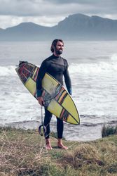 Satisfied male surfer with board smiling on grassy seasho